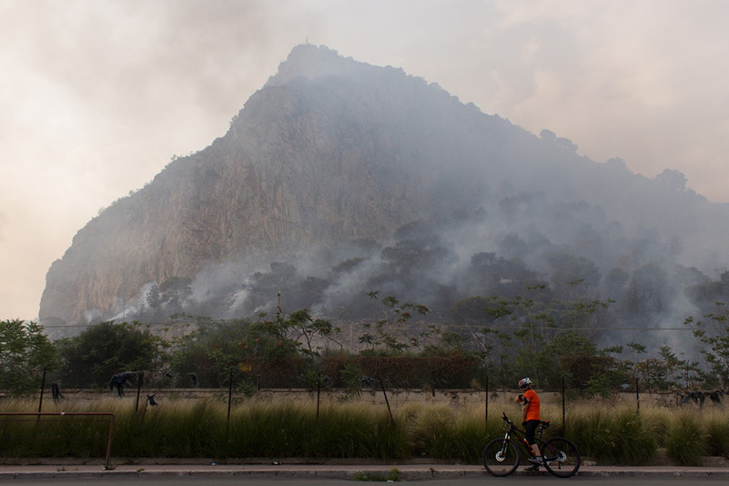 Un ciclista prende fiato durante un incendio di Monte Pellegrino a Palermo